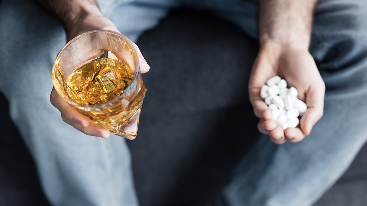 A man with a drink in one hand and a mountain of pills in the other. Combining alcohol and benzodiazepines can lead to memory problems