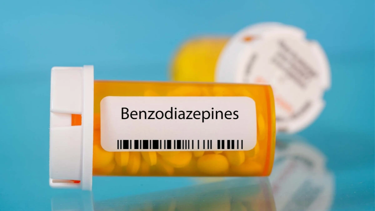 Yellow pill bottle with pills inside. The pill bottle is labeled "Benzodiazaphines"
