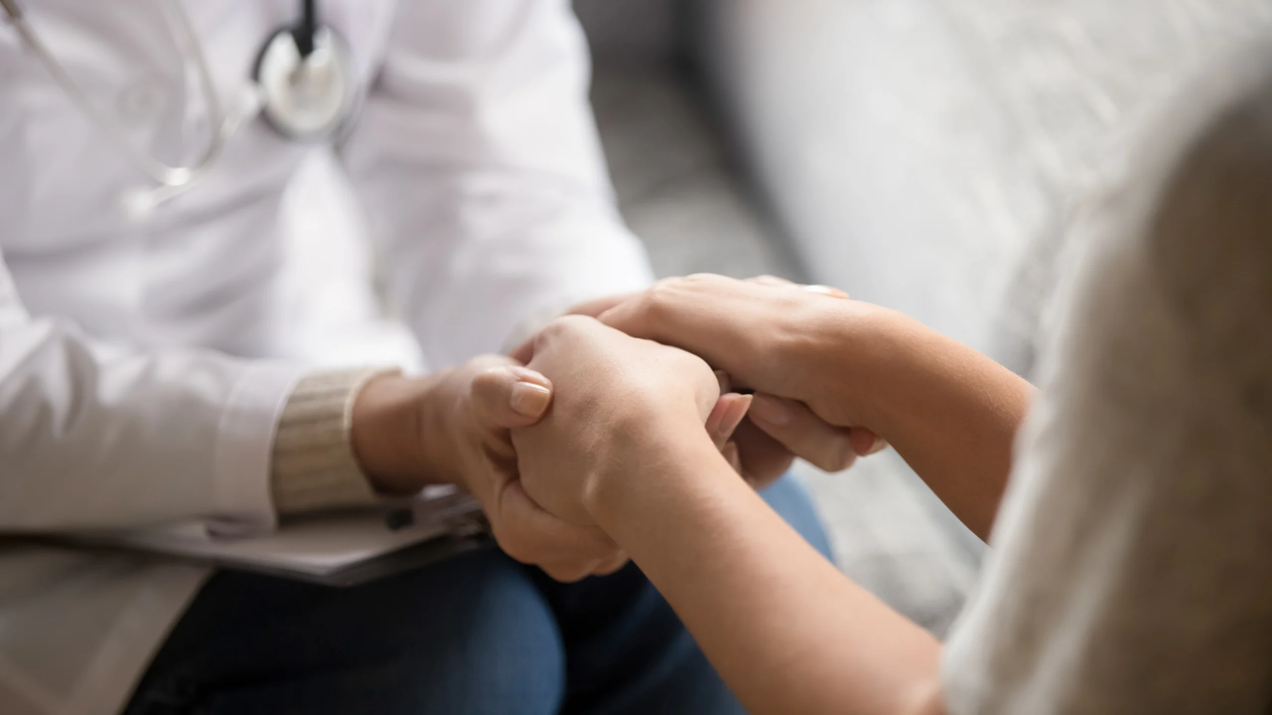 A close-up shot shows a healthcare professional in a white coat holding hands with a patient.