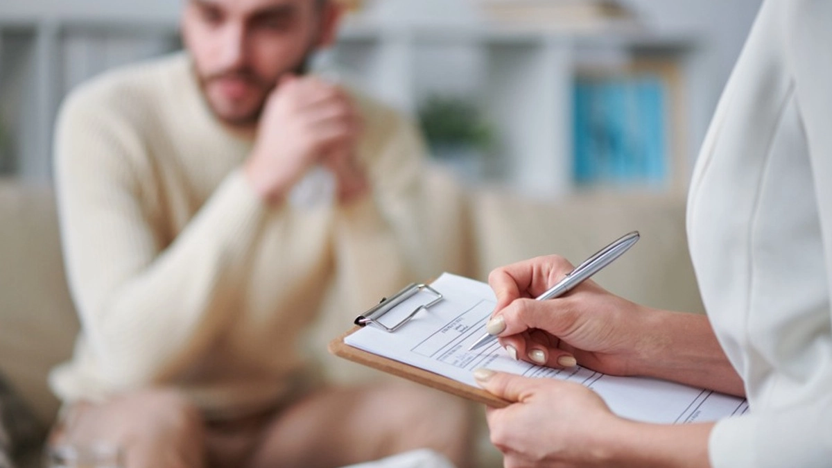 therapist writing on a clipboard with a concerned client in front of him