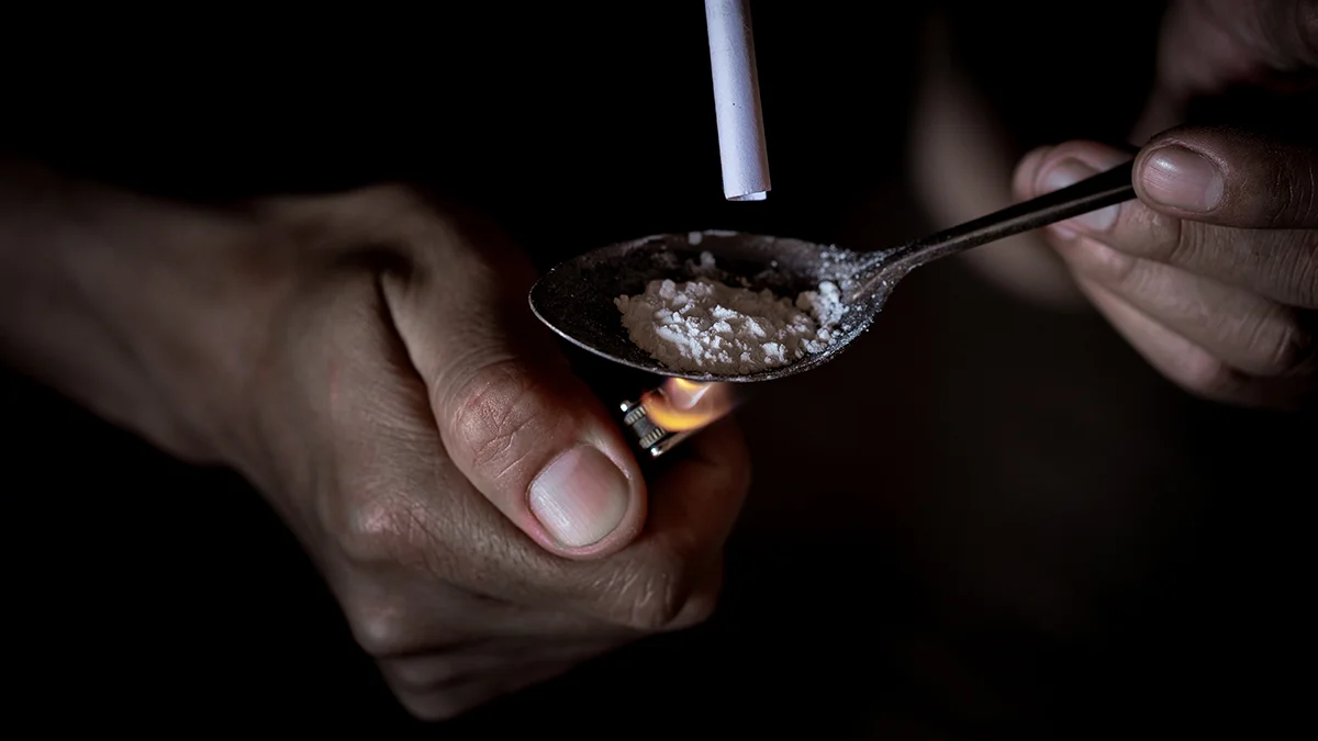 person smoking heroin by lighting a spoon full of it